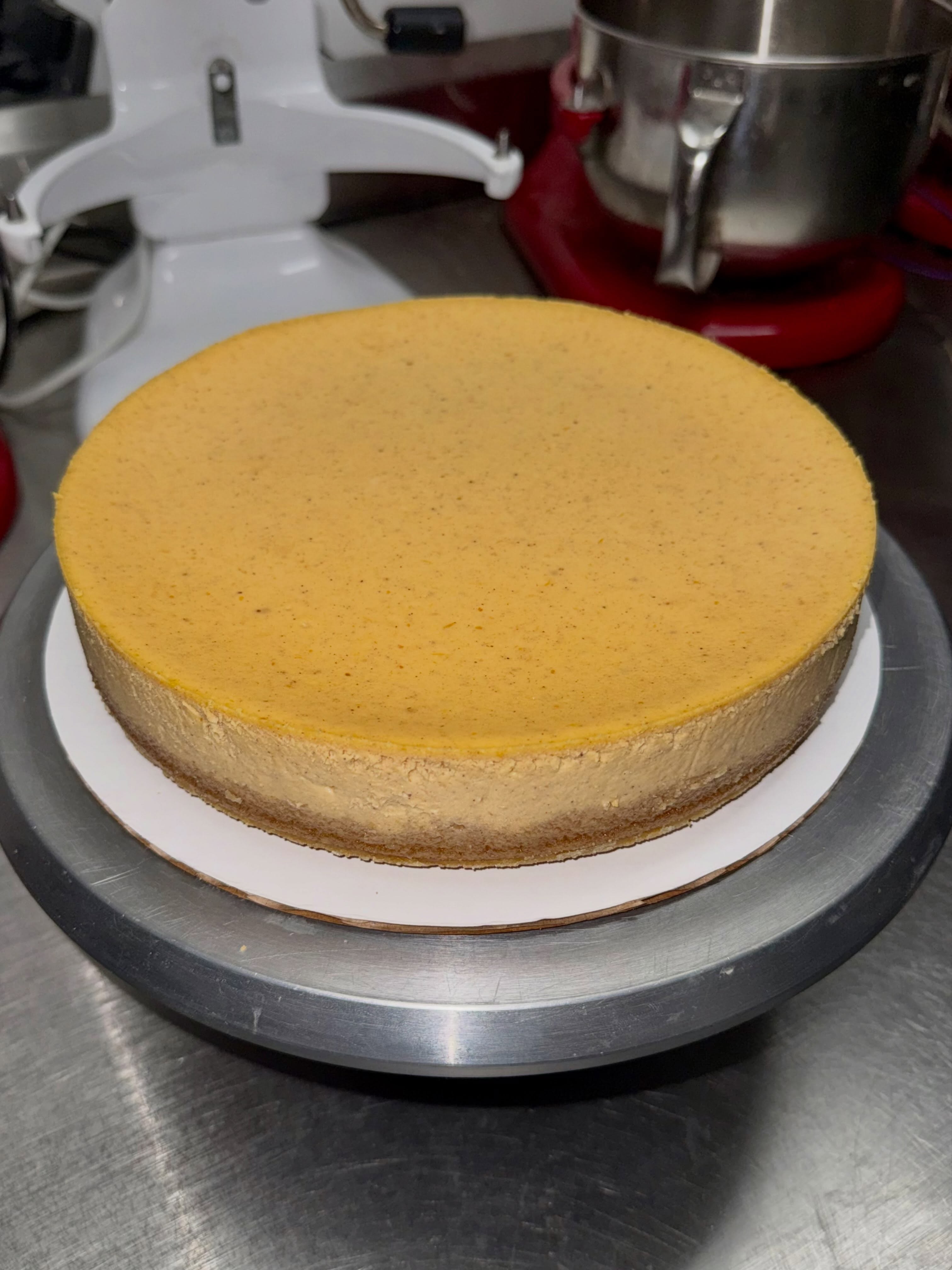 Whole pumpkin cheesecake made by Fred Tauro, on a cake stand in the bakery kitchen.